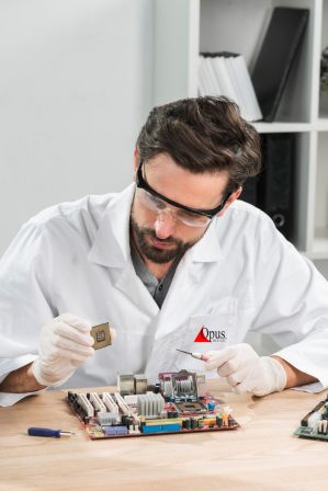 technician-holding-computer-chip-with-motherboard-wooden-desk